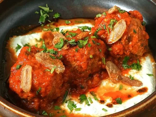 Three meatballs in red sauce on creamy base with herbs and slivers.
