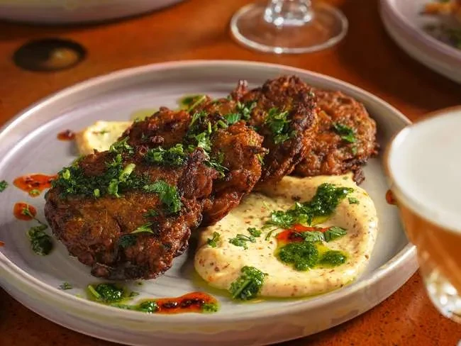 Plated golden-brown fried patties with herbs, creamy puree, and colorful drizzles.