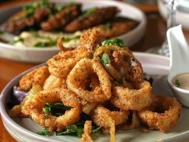 Golden-brown fried rings with black pepper, green herbs, and leafy vegetables.