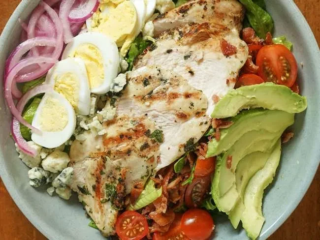 Vibrant, artfully arranged salad with chicken, eggs, avocado, tomatoes, blue cheese.