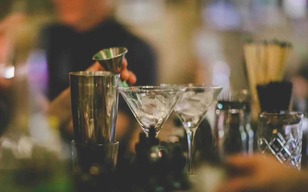 Bartender preparing a drink with martini glasses and shaker on a bar.