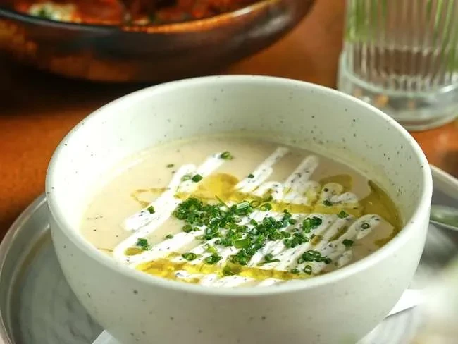 Creamy soup in white bowl with chives, olive oil, and white sauce.