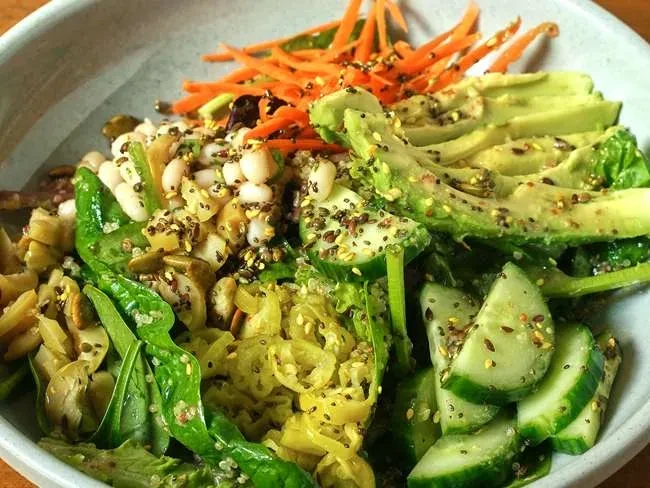 Vibrant salad bowl with avocado, carrots, white beans, and leafy greens.