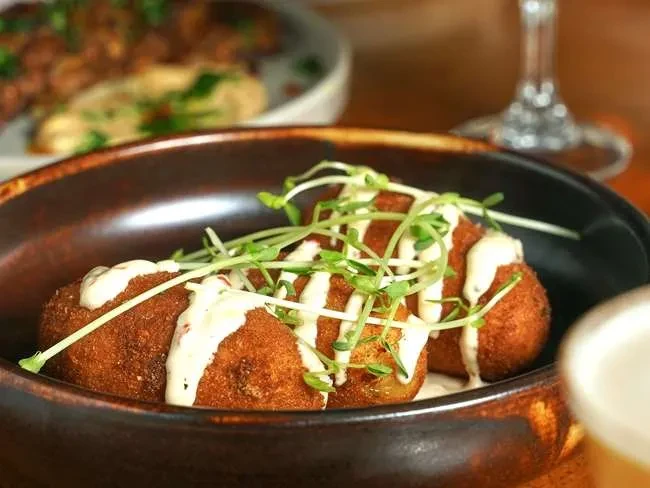 Oval fried croquettes with creamy white sauce and green microgreens in a bowl.