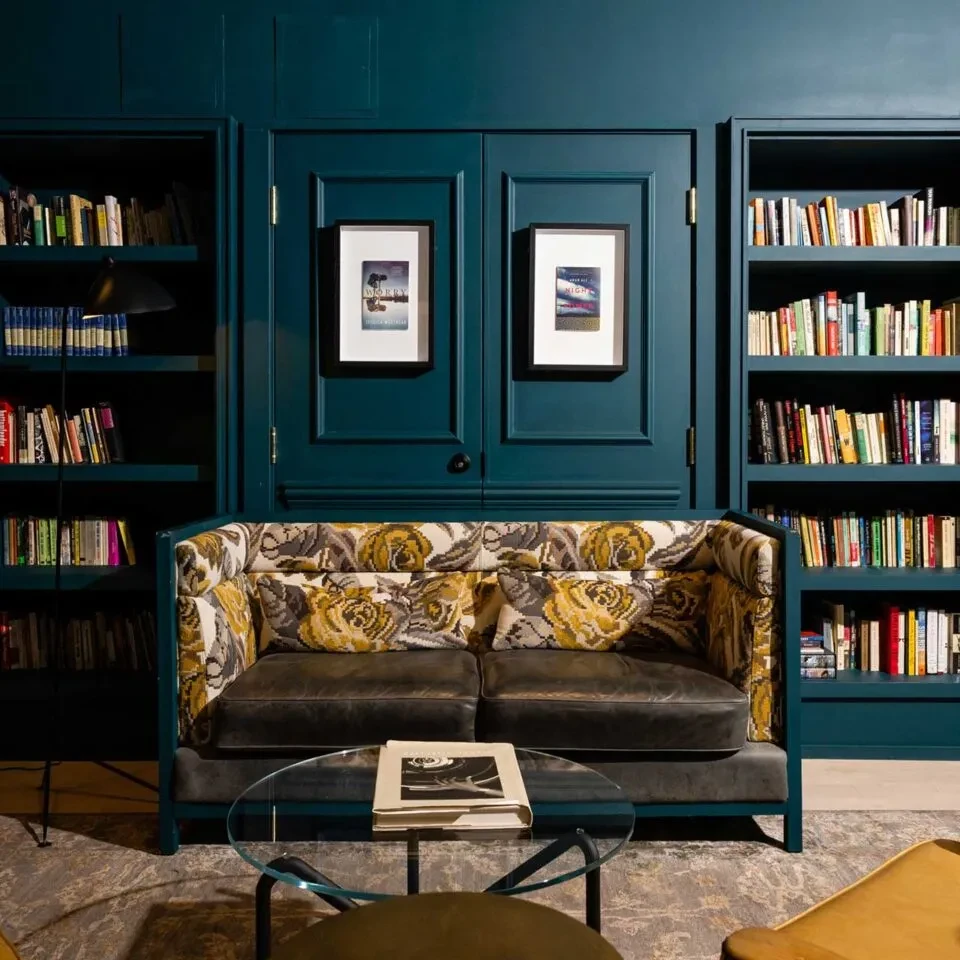 Teal lounge with rose-patterned sofa, coffee table, and bookshelves.