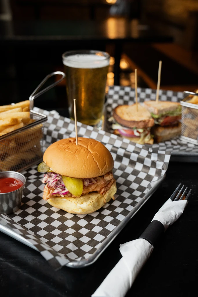 Fried chicken sandwich with coleslaw, fries, ketchup, and beer.