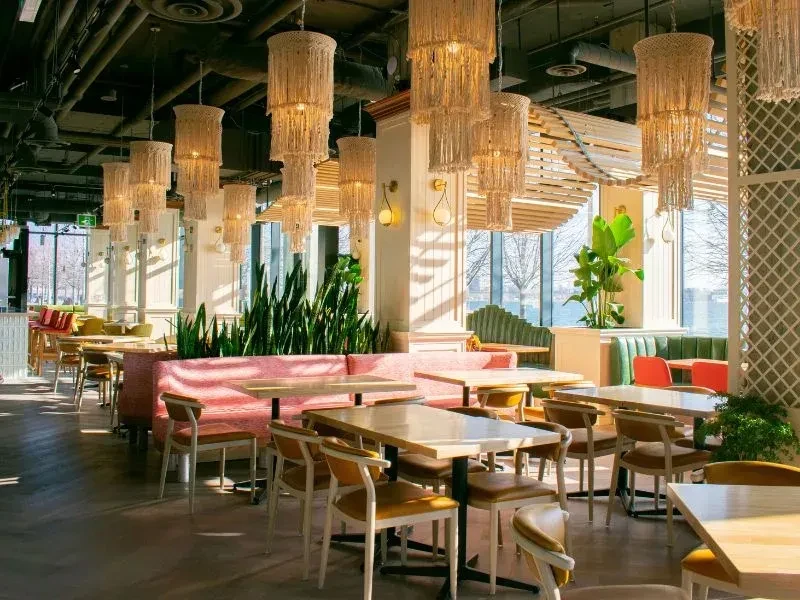 Bright modern restaurant with pink booth, macrame chandeliers, water view.