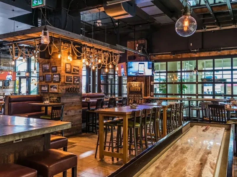 Industrial-rustic bar interior with varied seating and shuffleboard table.