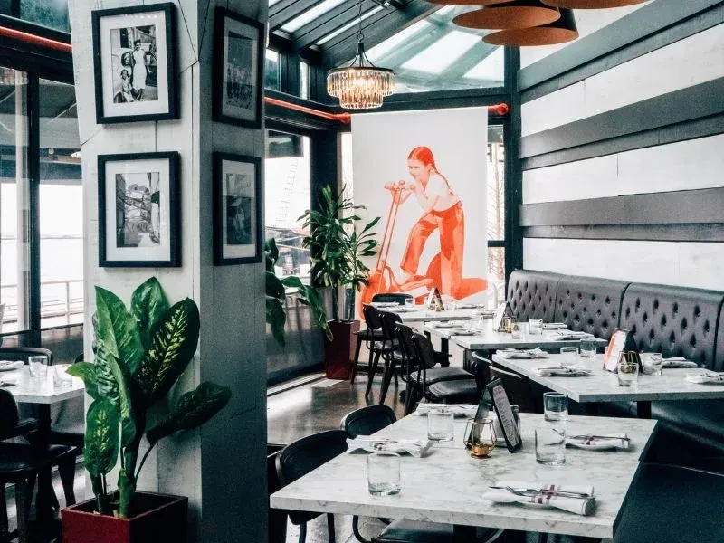 Modern restaurant interior with marble tables, dark leather seating, and bright light.