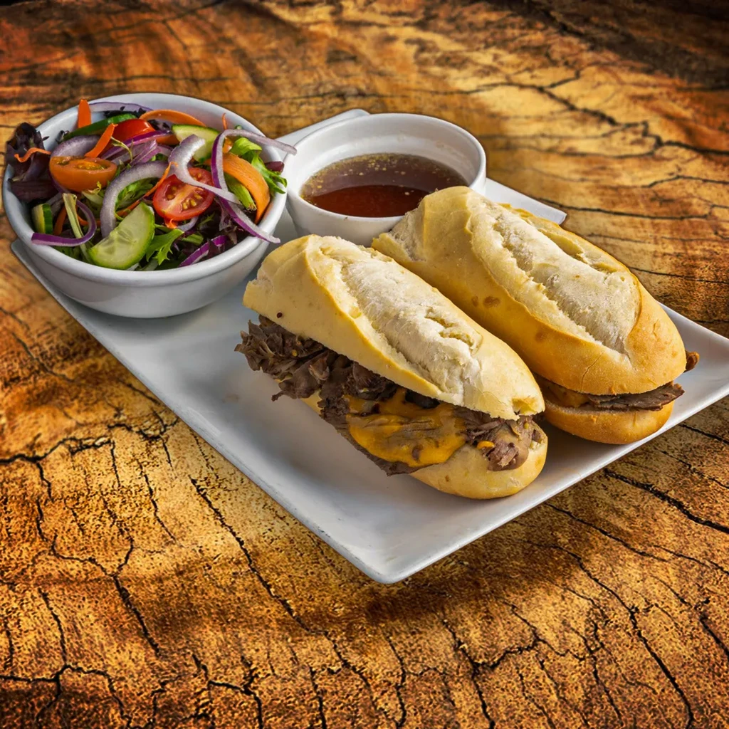 Oblong meat and cheese sandwiches with salad and au jus.