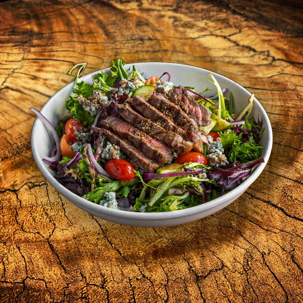Medium-rare steak salad with mixed greens, tomatoes, and blue cheese crumbles.
