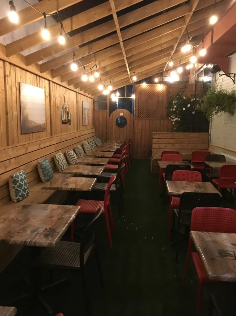 Restaurant interior with wooden beams, string lights, banquette, green floor.