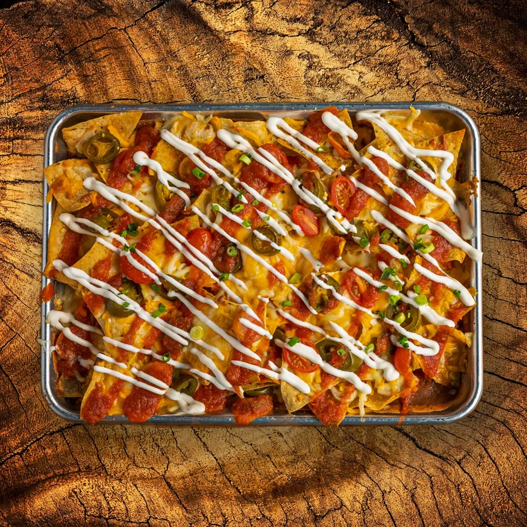 Tray of nachos with melted cheese, salsa, jalapeños, and drizzled sour cream.