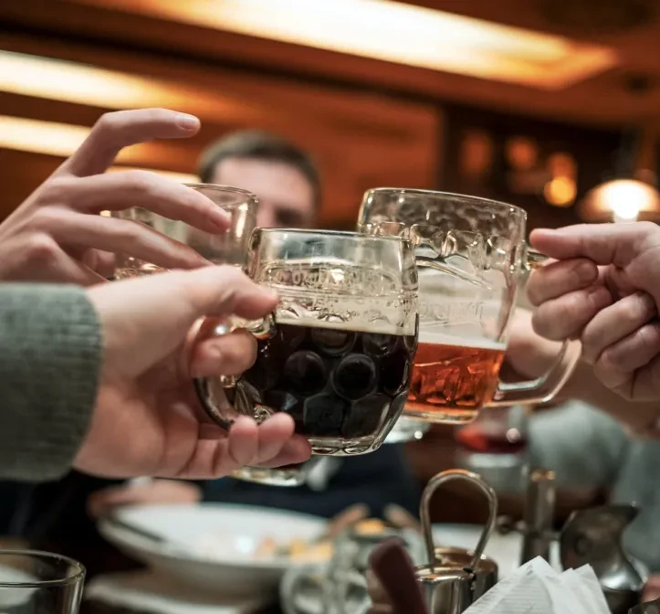Four hands clinking beer steins in a warm bar setting.