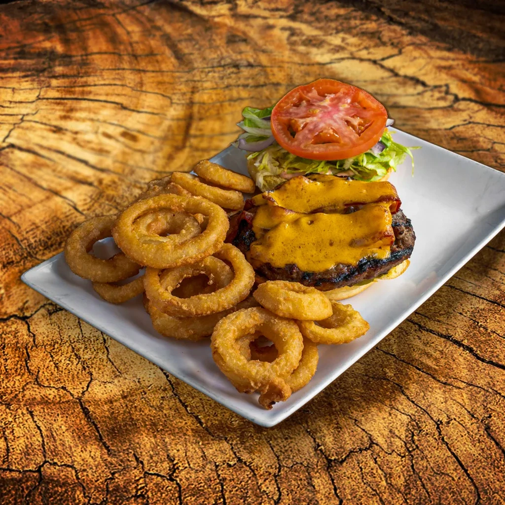 Grilled burger with cheese, bacon, and onion rings on rustic wood.