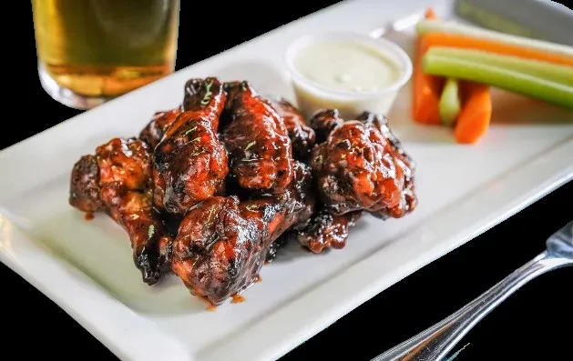 Plate of glazed chicken wings, dipping sauce, vegetables, and beer.