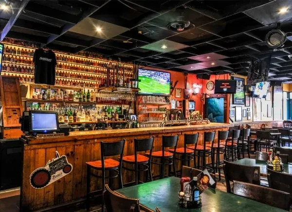 Vibrant bar interior with stocked counter, orange stools, and soccer game on TV.