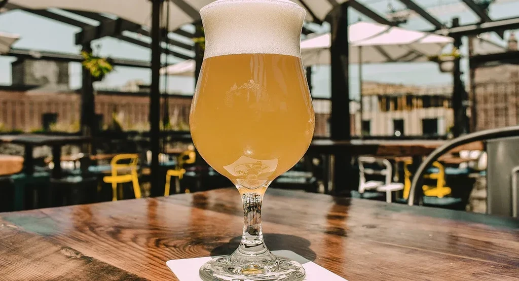 Hazy yellow beer with a frothy white head on a wooden table.