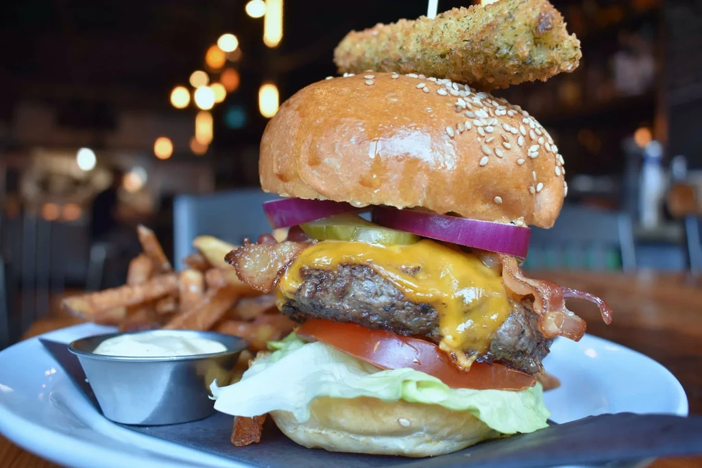 Stacked burger with fried pickle spear, french fries, and dipping sauce.