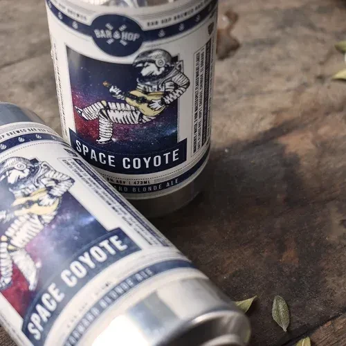 Two Space Coyote beer cans on wood with an astronaut coyote label.