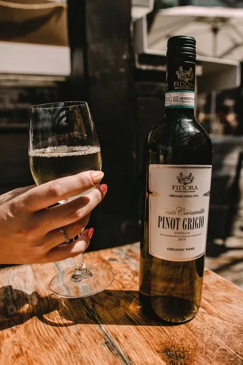 Organic Fidrora Pinot Grigio bottle and wine glass on wood table.