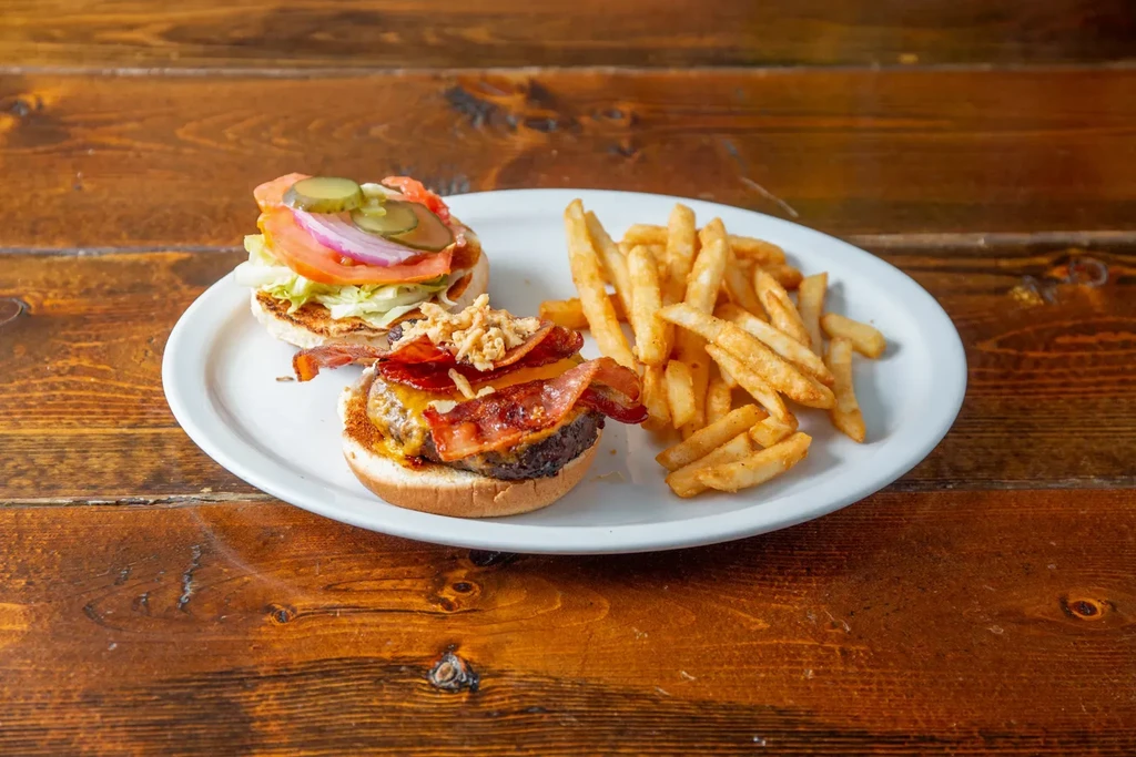 Open-faced burger with bacon, cheese, and fries on a wooden table.