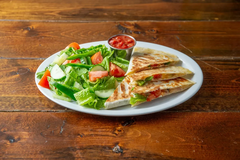 A plate of garden salad, quesadillas, and salsa on a wooden table.