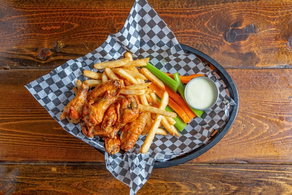 Basket of wings, fries, veggies, and dip on a wood table.