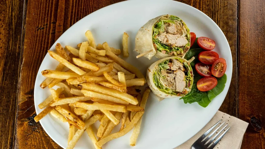 Chicken wrap, french fries, cherry tomatoes, and spinach on a plate.