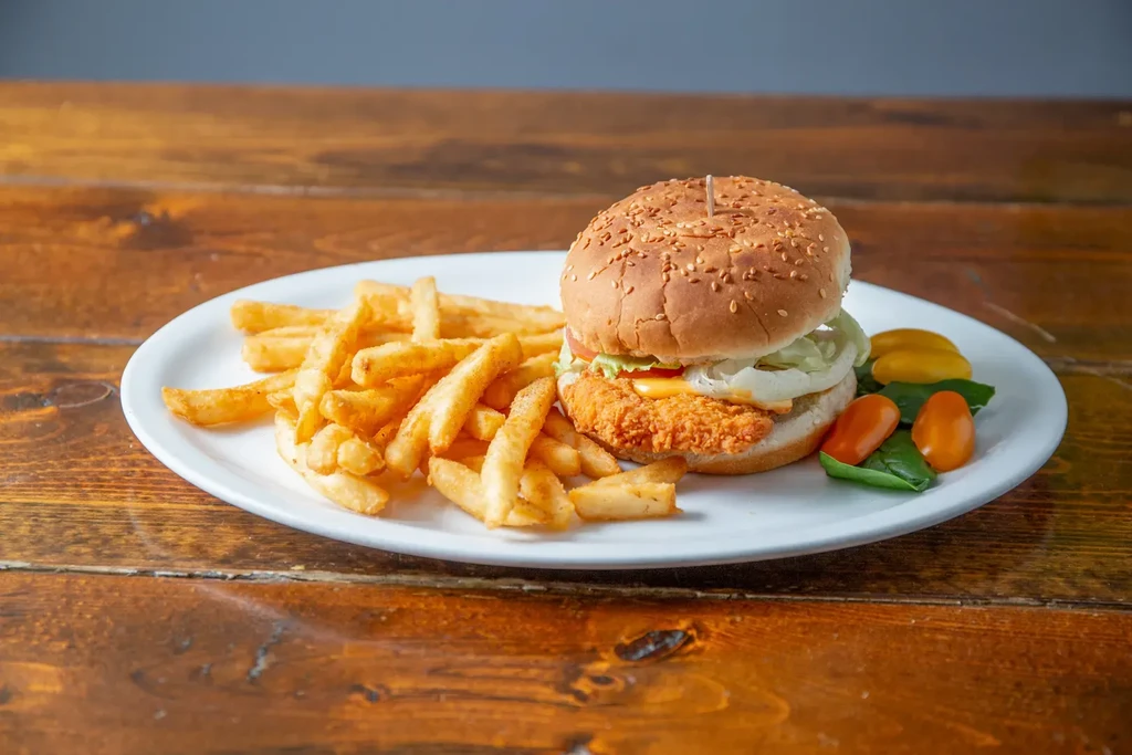 Fried burger, golden fries, and fresh greens on a rustic table.