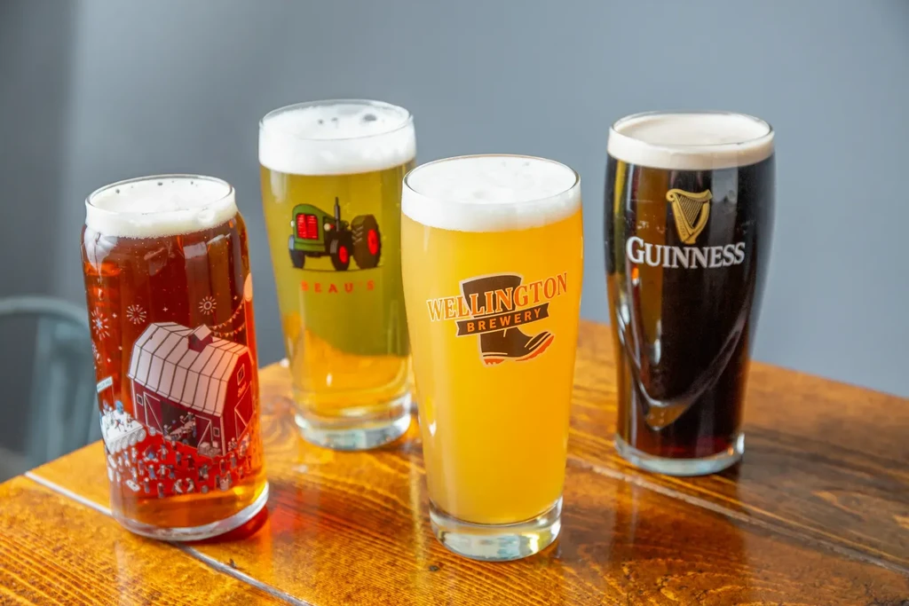 Four distinct branded beers in glasses on a wooden table.