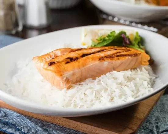 Grilled salmon on white rice, garnished with lettuce and a lemon slice.