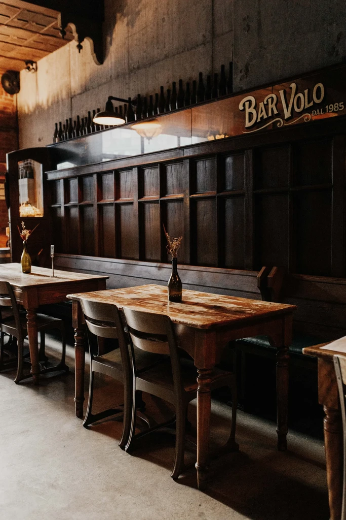 Rustic bar interior with wooden tables, booth, and "BAR VOLO" sign.