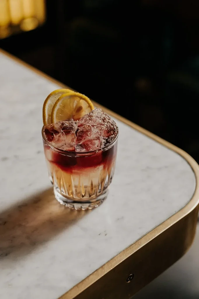 Layered amber and red cocktail with crushed ice and lemon on marble.