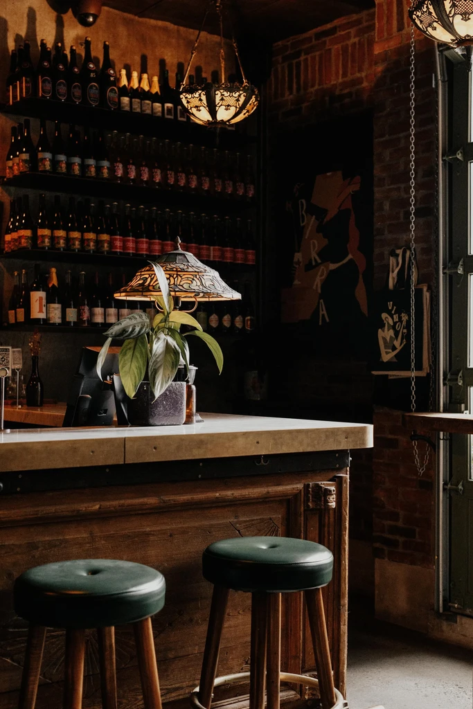 Rustic bar interior with a wooden counter, two stools, and many bottles.