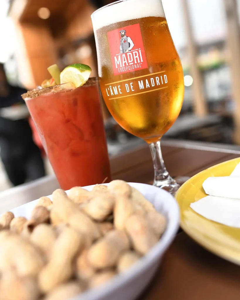 Close-up of a Bloody Mary, Madri beer, and peanuts on a table.