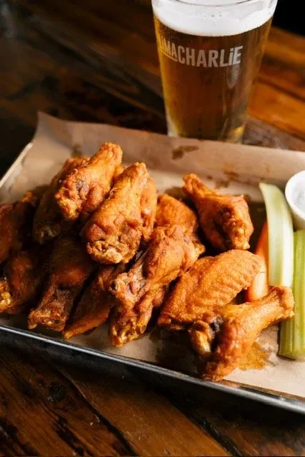 Tray of crispy fried chicken wings, fresh vegetables, sauce, and beer.