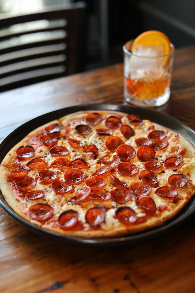Pepperoni pizza with melted cheese, red pepper flakes, and a cocktail.