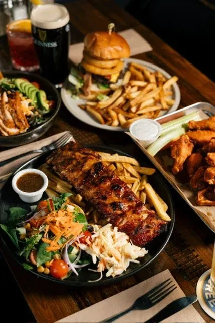 High-angle shot of a table with BBQ ribs, burger, wings, and drinks.