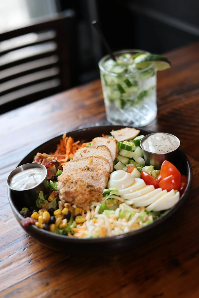 Grilled chicken Cobb salad with eggs and vegetables on a dark table.