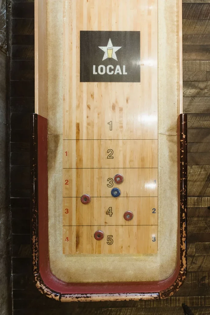 Wooden shuffleboard table with a "LOCAL" star logo and scattered game pucks.