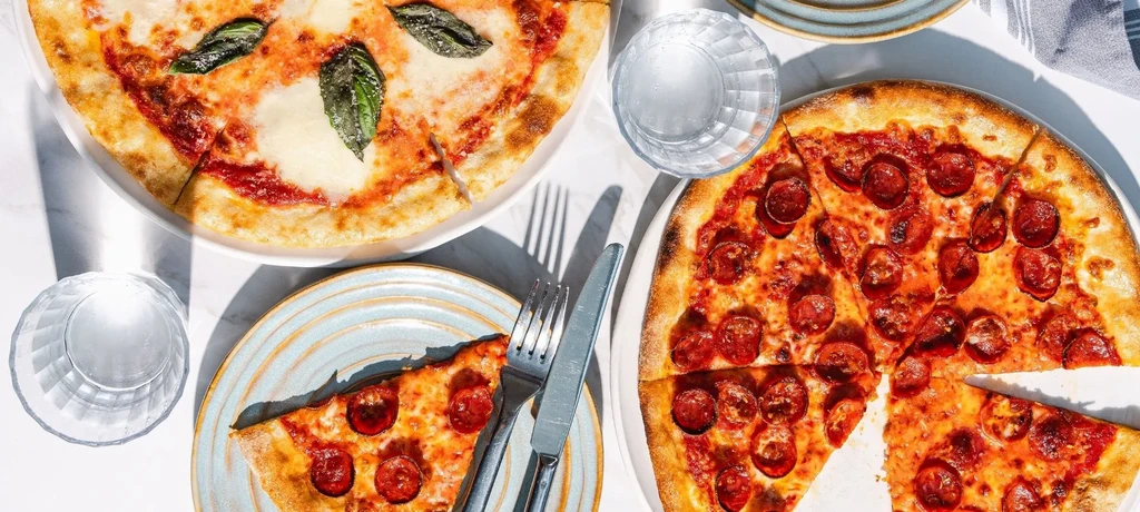 Overhead view of Margherita and pepperoni pizzas, one slice removed.