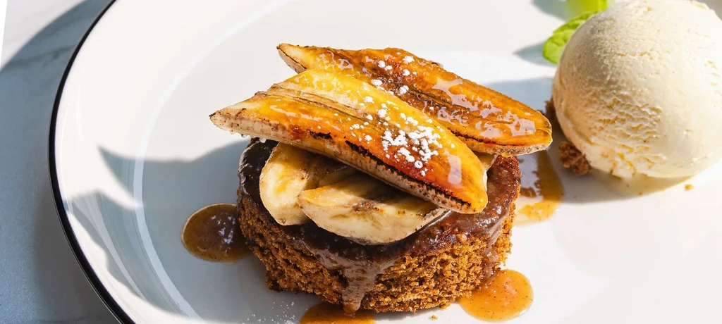 Caramelized banana dessert with vanilla ice cream, crumbs, and brown sauce.