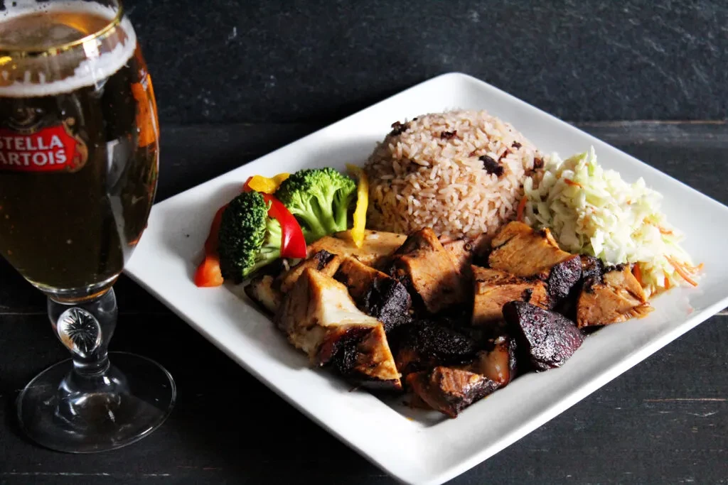 Roasted meat, rice, vegetables, coleslaw, and Stella Artois beer.
