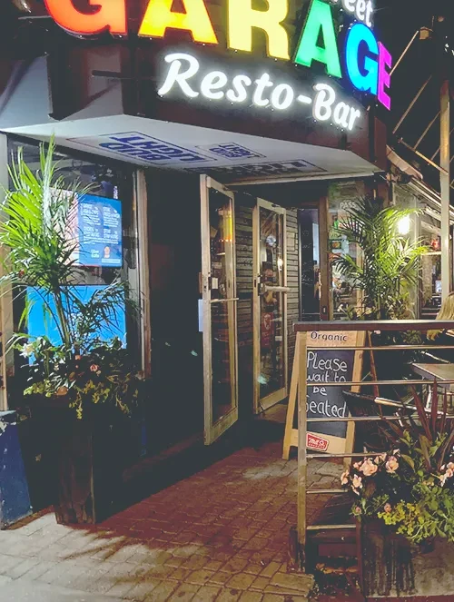 Exterior of GARAGE Resto-Bar at night, with multi-colored neon sign.