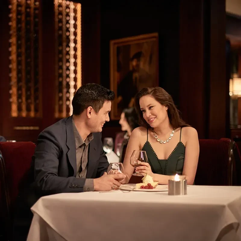 Smiling couple dines at an upscale restaurant with dessert, drinks, candle.