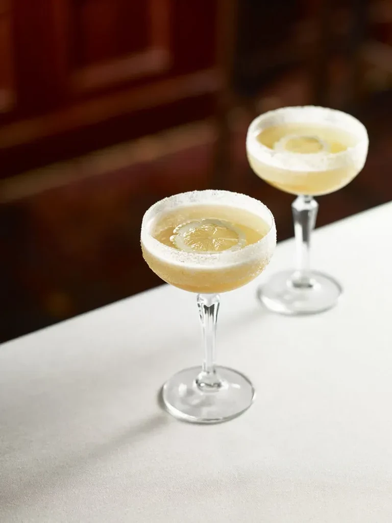 Two pale yellow cocktails with sugared rims and lemon slices.