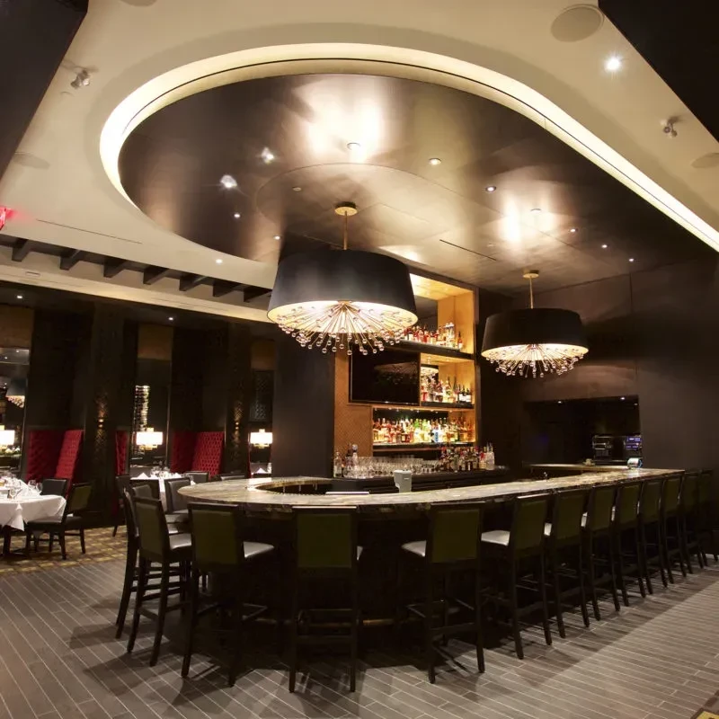 Modern restaurant interior featuring curved bar, chandeliers, and dining area.
