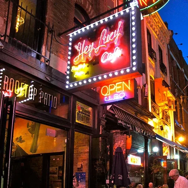 Hey Lucy Cafe building at night, glowing with neon signs and patio.