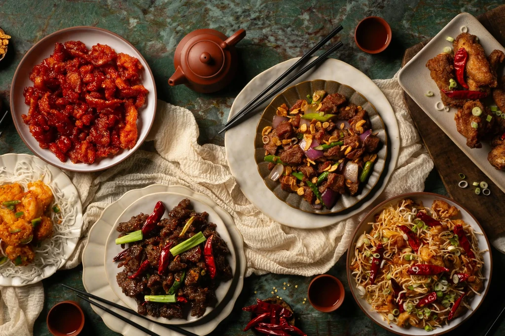 Five Asian dishes, tea, and chopsticks on a dark marbled table.